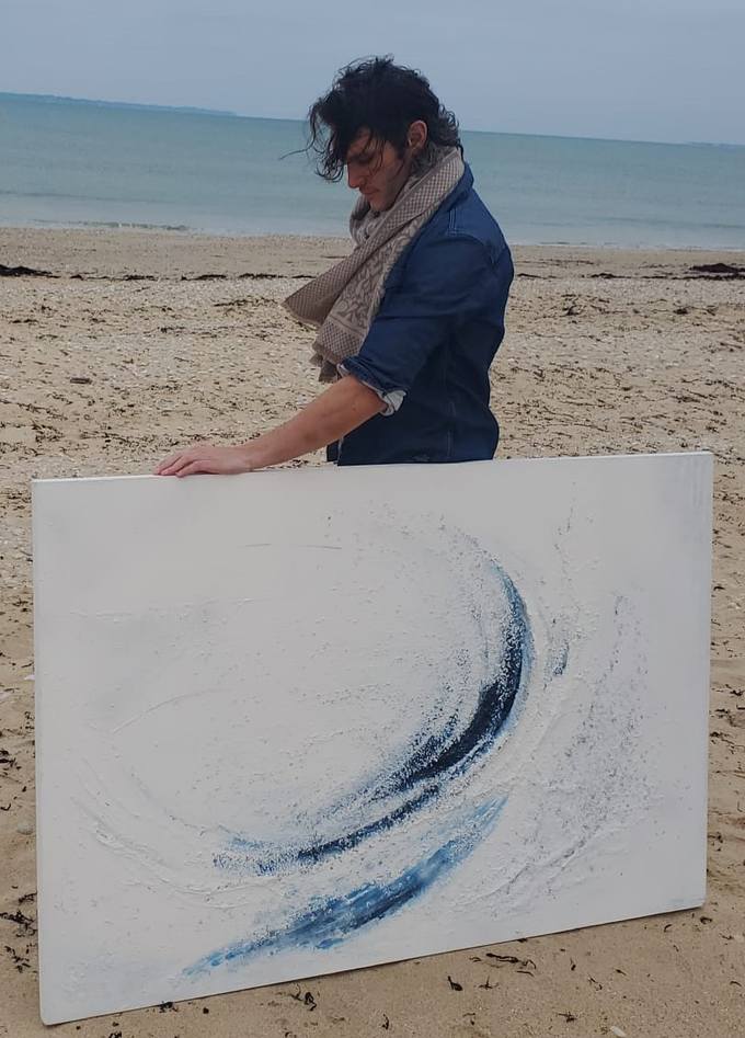 Werner Wilfred sur une plage bretonne avec une toile en relief bleu et blanc.